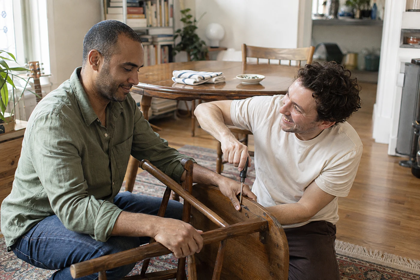 Two men repairing a wooden chair together at home.